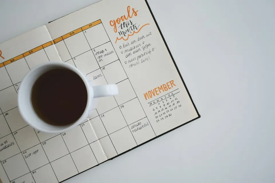 An open planner with a calendar spread and a pen on a wooden desk, ready for a No Spend November tracker.